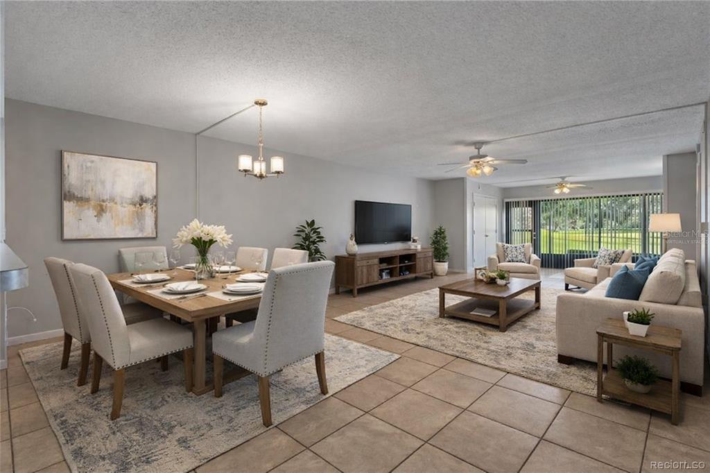 An open-concept living and dining room features tile flooring, neutral furniture, and a large window — 3 CYPRESS RUN UNIT 35A, HOMOSASSA, FL