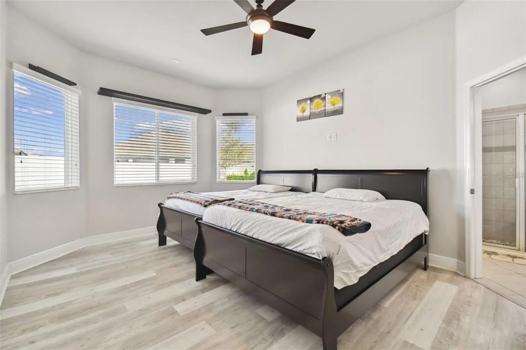 A bedroom features light wood-look flooring, white walls, a ceiling fan, and two dark-framed beds — 2776 SATILLA LOOP, ODESSA, FL