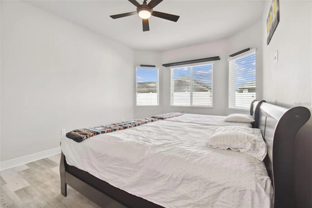 A bedroom with light gray walls, wood-look flooring, a ceiling fan, and a large bed — 2776 SATILLA LOOP, ODESSA, FL
