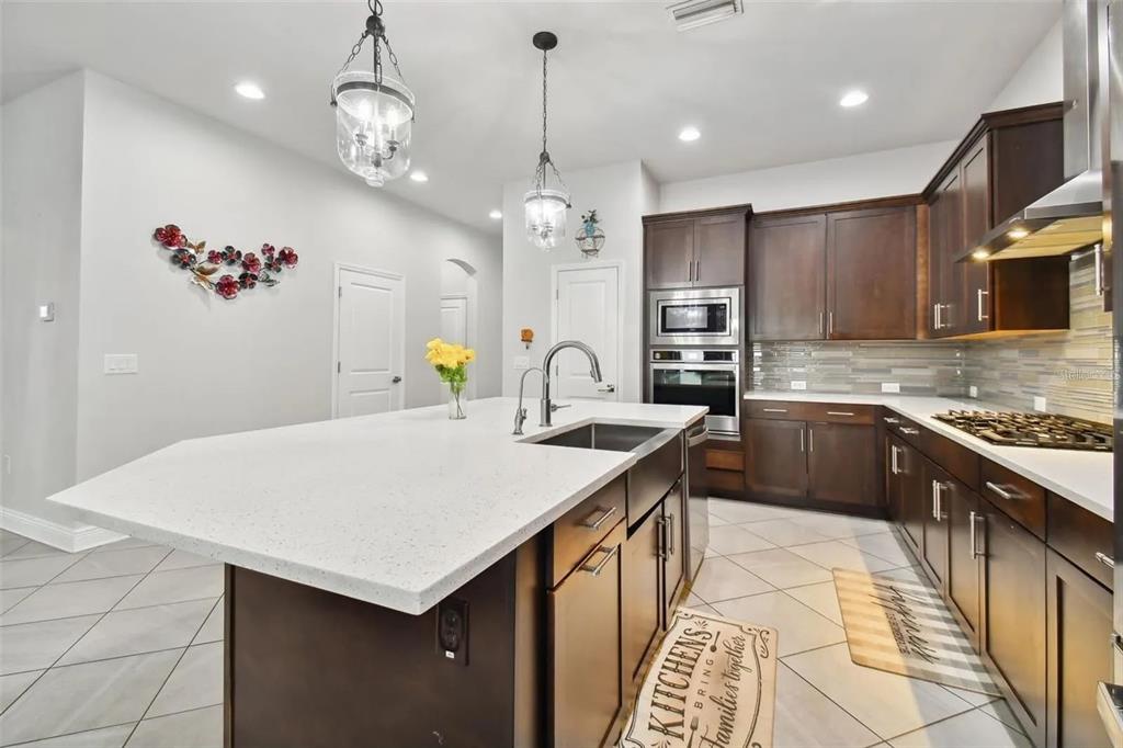 A kitchen features dark wood cabinets, a large white quartz island, and tile flooring — 2776 SATILLA LOOP, ODESSA, FL