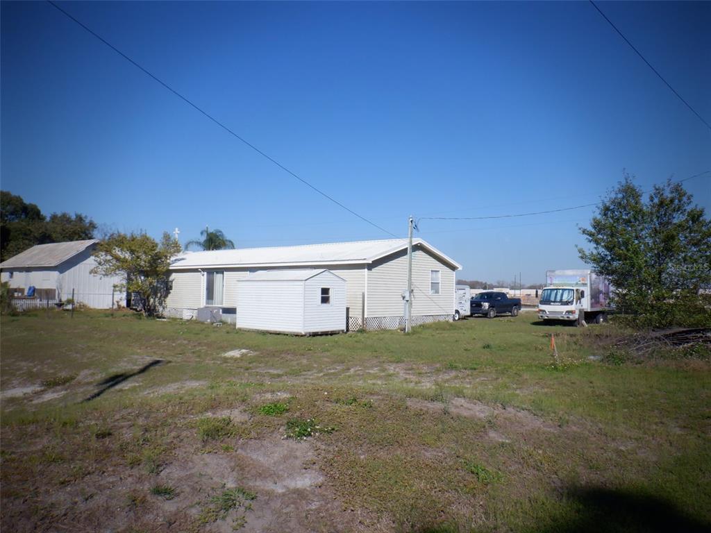 A light-colored manufactured home sits on a grassy lot with a small shed and vehicles — 2239 OLD GUNN HIGHWAY, ODESSA, FL