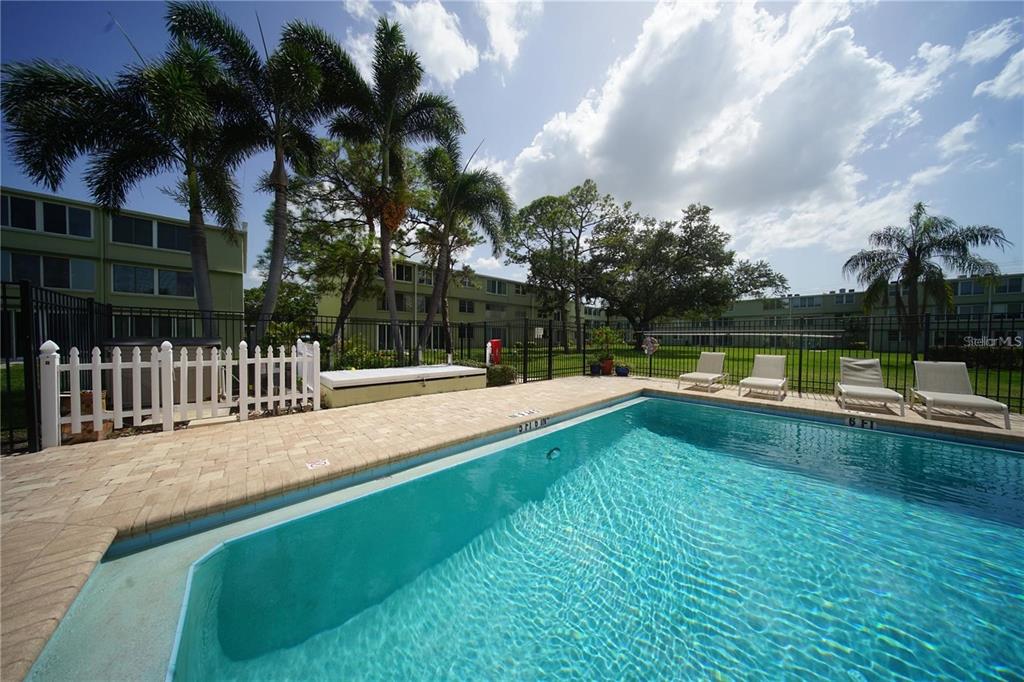 An outdoor swimming pool with lounge chairs and palm trees in a residential complex — 4705 1ST STREET NE UNIT 132, ST PETERSBURG, FL