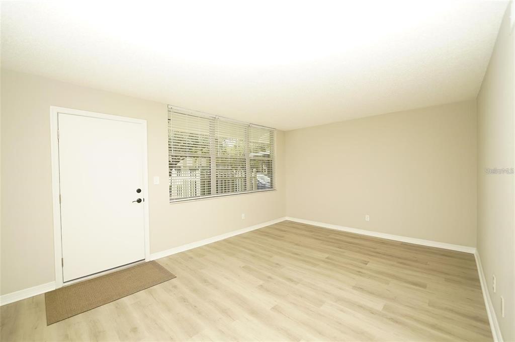 An empty room with light wood-look flooring, beige walls, a white door, and window blinds — 4705 1ST STREET NE UNIT 132, ST PETERSBURG, FL