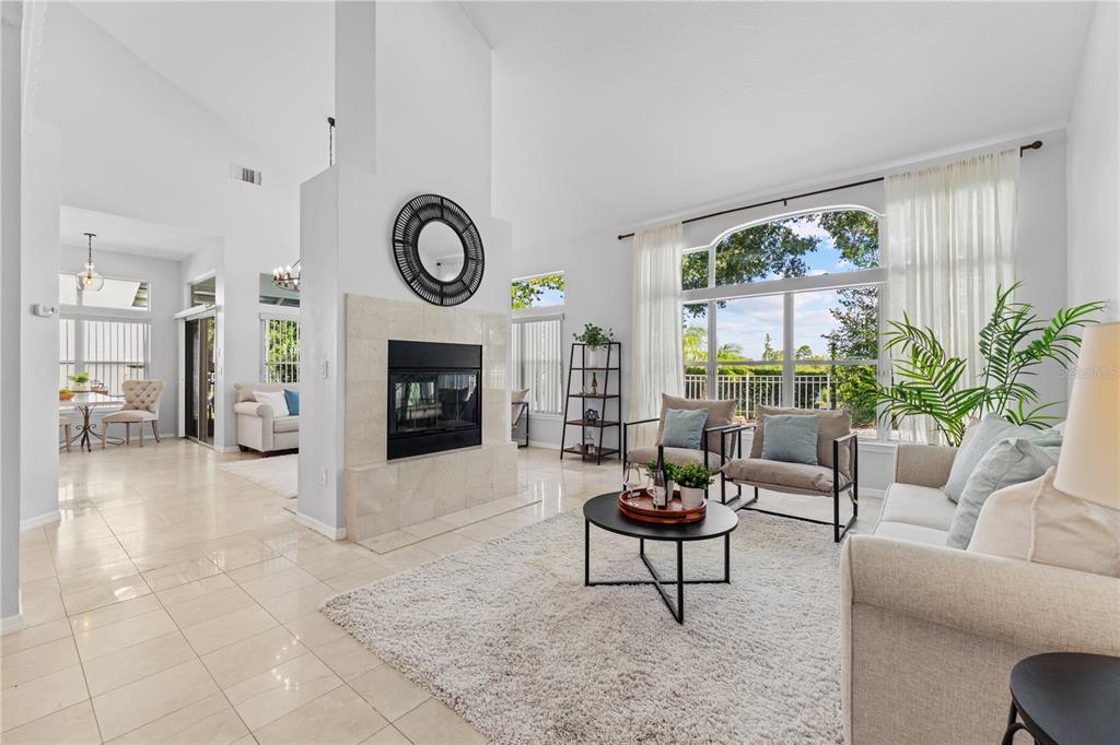 A bright living room features a central fireplace, tile flooring, and large windows with views — 130 WIMBLEDON CIRCLE, LAKE MARY, FL