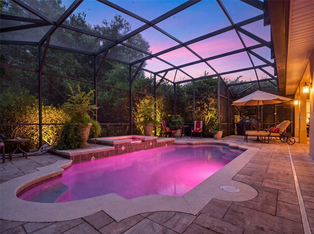 A screened-in pool and spa area with stone pavers and outdoor furniture at dusk — 10908 PRIEBE RD, CLERMONT, FL