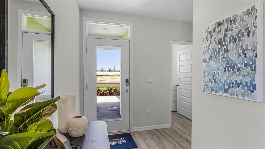 An entryway features a glass-paneled front door, light wood flooring, and a blue abstract painting — 5584 TAVERNA LOOP, WINTER HAVEN, FL