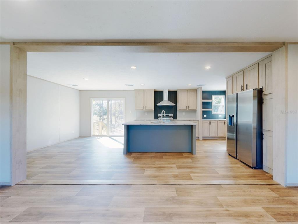 A kitchen features a blue island, light wood cabinets, stainless steel appliances, and wood-look flooring — 660 NE 131 AVENUE, WILLISTON, FL