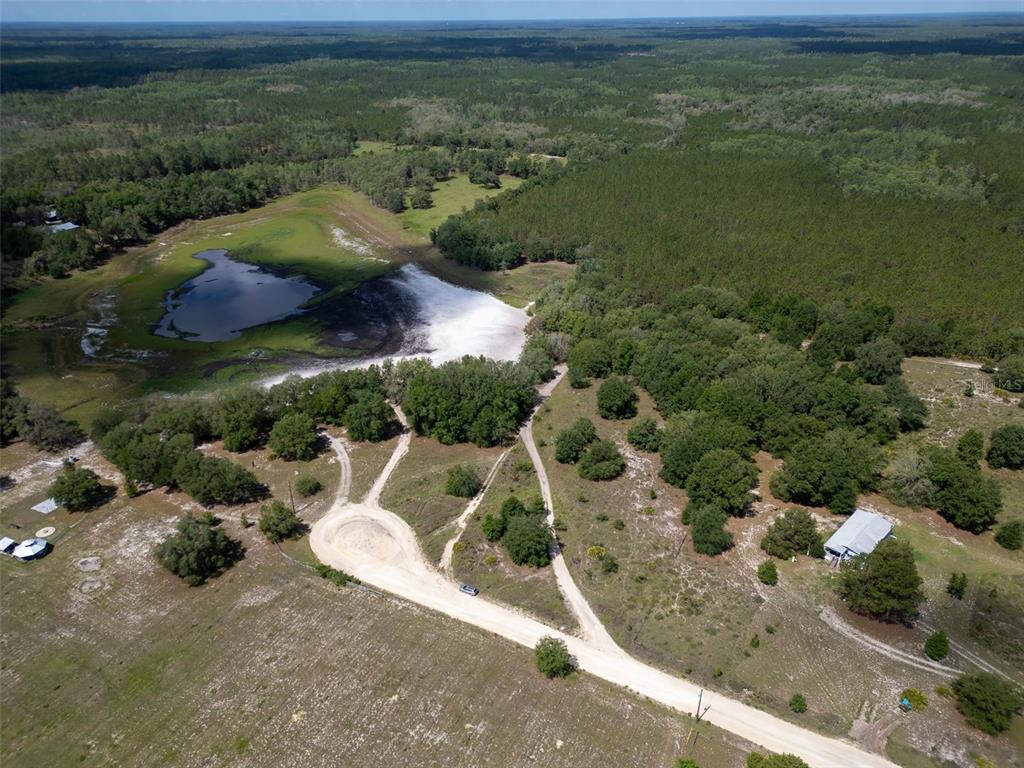 An aerial view shows a dirt road, a small pond, and wooded areas on rural land — SE 53 COURT, TRENTON, FL