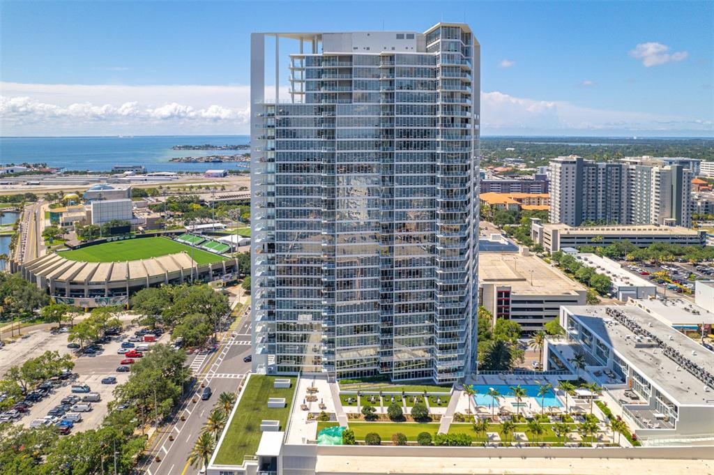 An aerial view of a tall residential skyscraper surrounded by city buildings and parking lots — 175 1ST STREET S UNIT 1204, ST PETERSBURG, FL
