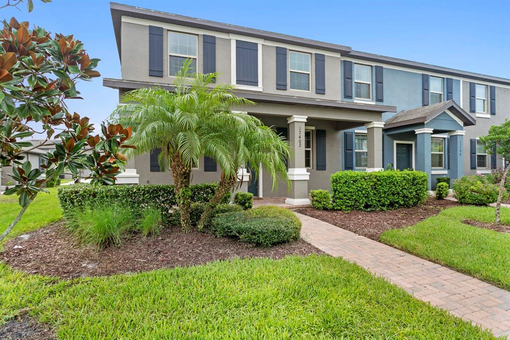 A two-story townhouse with a covered front porch, palm tree, and brick walkway — 17402 CRUISER BEND, LAND O LAKES, FL