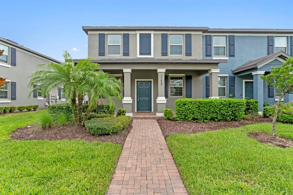 A two-story townhouse with a brick walkway, covered front porch, and manicured landscaping — 17402 CRUISER BEND, LAND O LAKES, FL