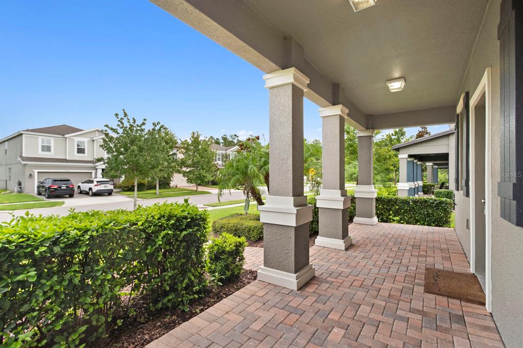 A covered front porch with brick pavers and square columns overlooks a suburban street — 17402 CRUISER BEND, LAND O LAKES, FL