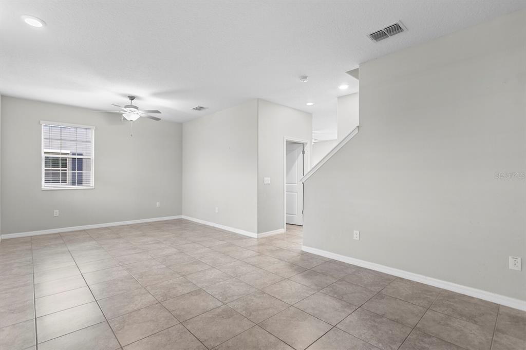An empty room with light gray walls, tile flooring, a ceiling fan, and a staircase — 17402 CRUISER BEND, LAND O LAKES, FL