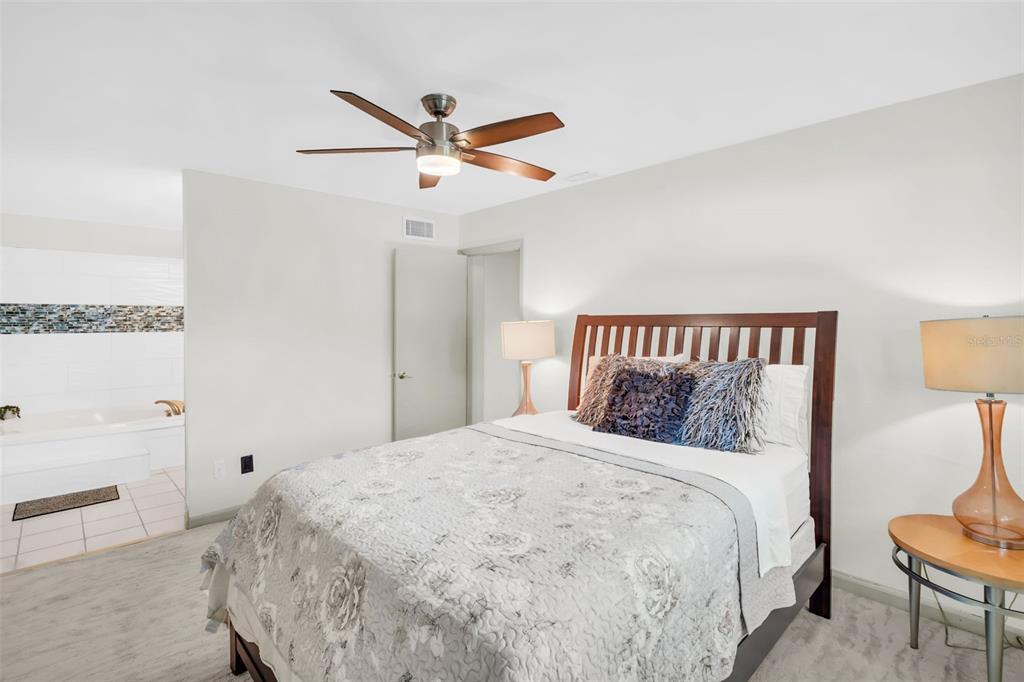 A bedroom features a queen bed, ceiling fan, and an open doorway to a bathroom — 1182 NORWOOD AVENUE, CLEARWATER, FL