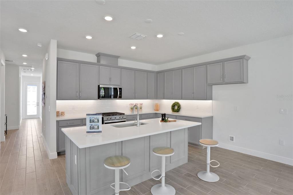A modern kitchen features gray cabinets, a white quartz island, and light wood-look tile flooring — 9124 WALCOTT LANE, LAKEWOOD RANCH, FL