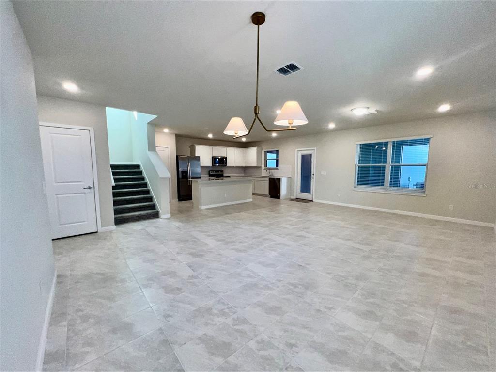 An open-concept living area features light tile flooring, a kitchen with white cabinets, and stairs — 6098 WINDY LEAF ALY, ST CLOUD, FL