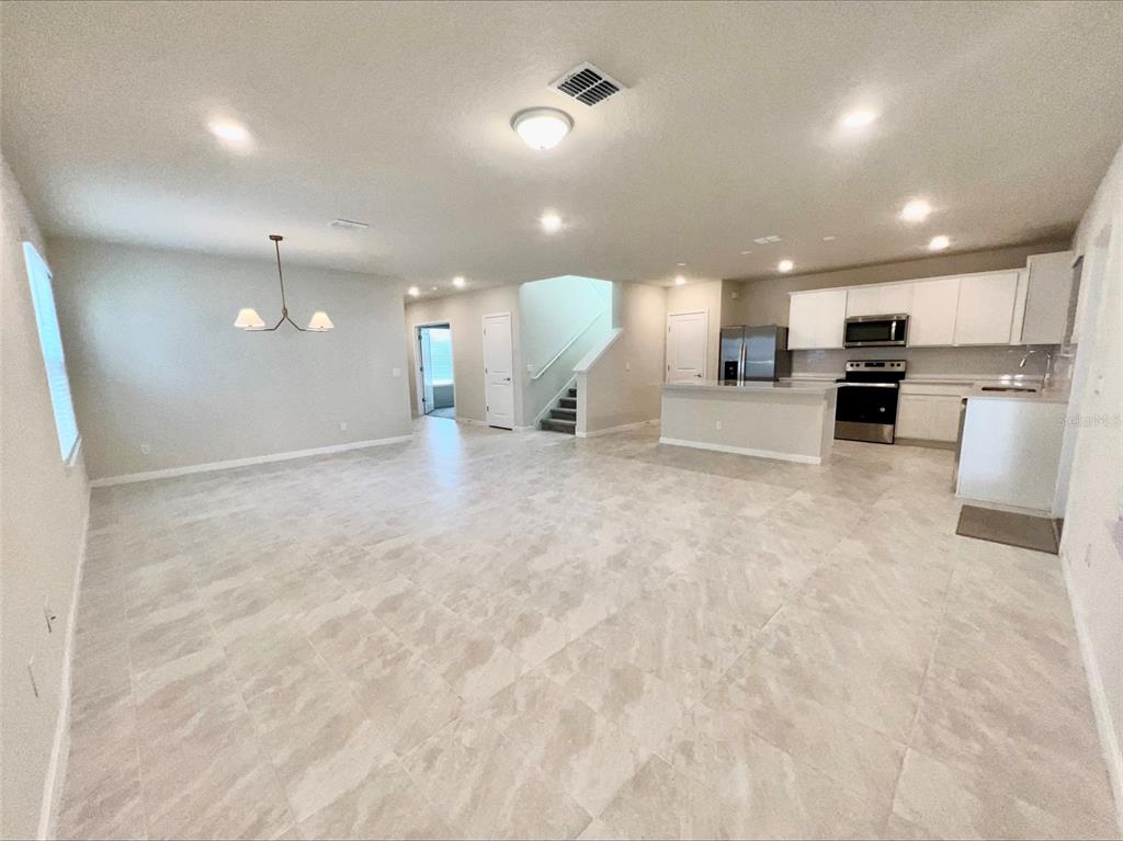 An open-concept kitchen and living area features light tile flooring and white cabinetry — 6098 WINDY LEAF ALY, ST CLOUD, FL