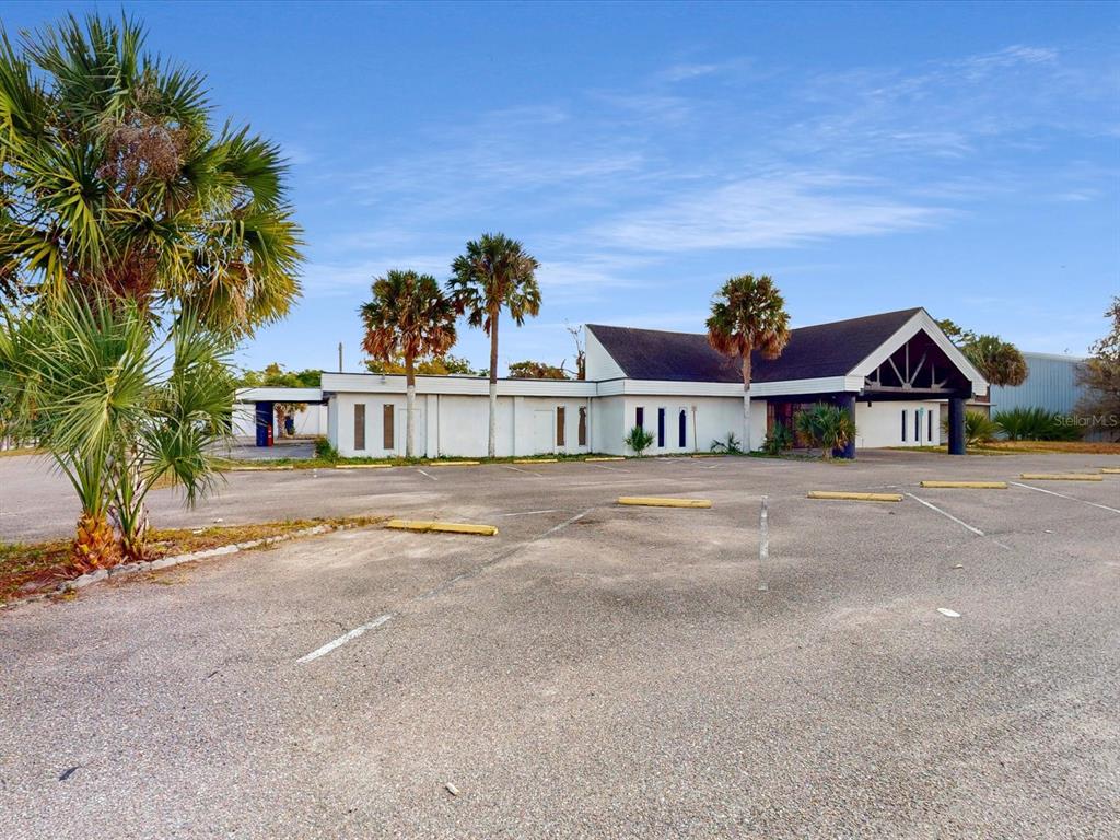 A white commercial building with a dark roof stands behind a large asphalt parking lot — 3425 FORSYTH ROAD, WINTER PARK, FL