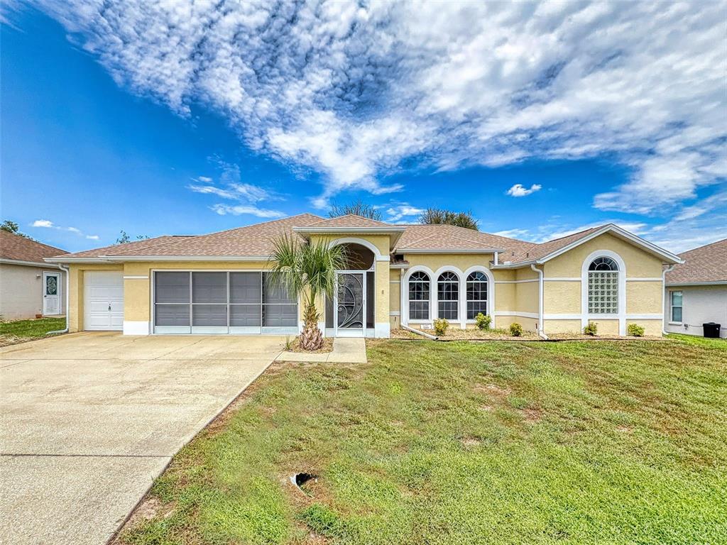 A single-story yellow house with a screened garage, arched windows, and a concrete driveway — 2089 NW 50TH CIRCLE, OCALA, FL