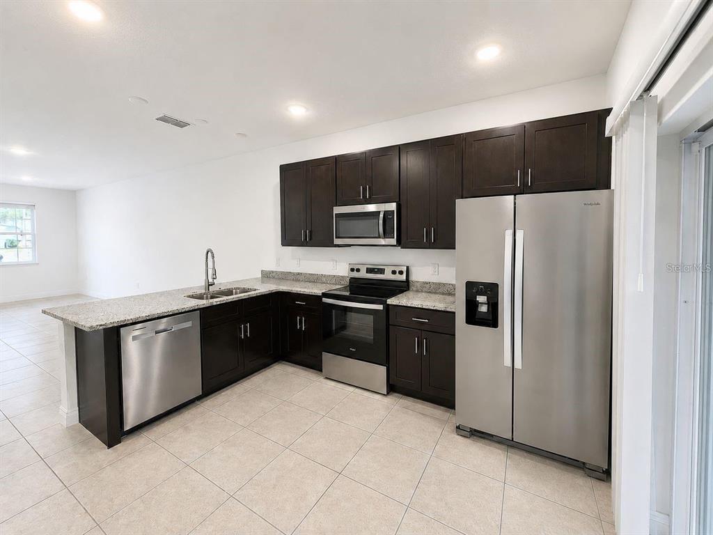 A kitchen features dark wood cabinets, granite countertops, and stainless steel appliances on tiled flooring — 13664 SW 61ST CIRCLE UNIT #2, OCALA, FL