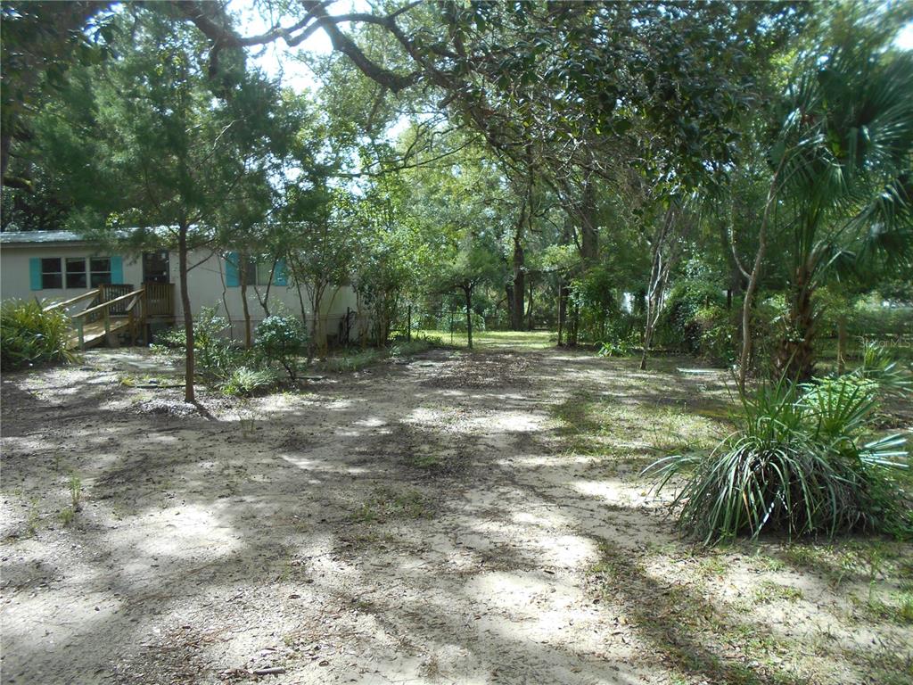 A sandy yard leads to a mobile home with a wooden ramp and blue shutters — 20425 NE 143RD STREET, SALT SPRINGS, FL