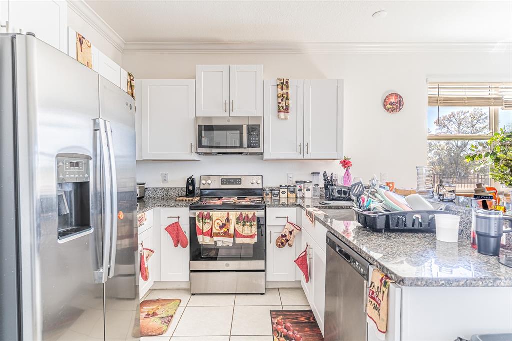 A kitchen features white cabinetry, stainless steel appliances, and granite countertops — 7014 RIPPLE POND LOOP, ZEPHYRHILLS, FL