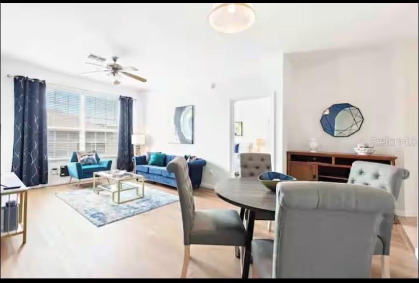 A living and dining area with light wood floors, a blue sofa, and a round table — 8103 COCONUT PALM WAY UNIT 302, KISSIMMEE, FL