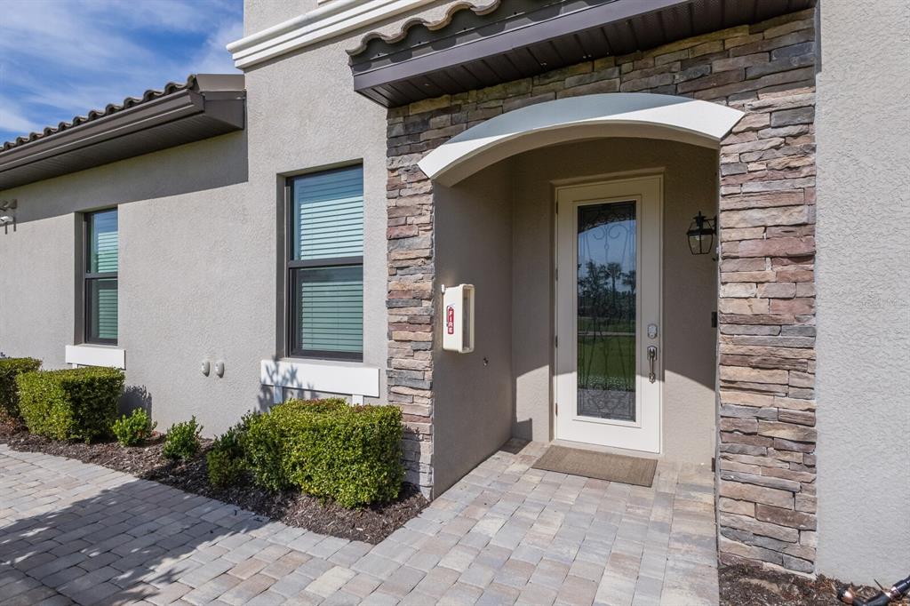 The exterior of a house features a stone-accented entryway, a glass-paneled door, and landscaping — 18117 GAWTHROP DRIVE UNIT 104, BRADENTON, FL