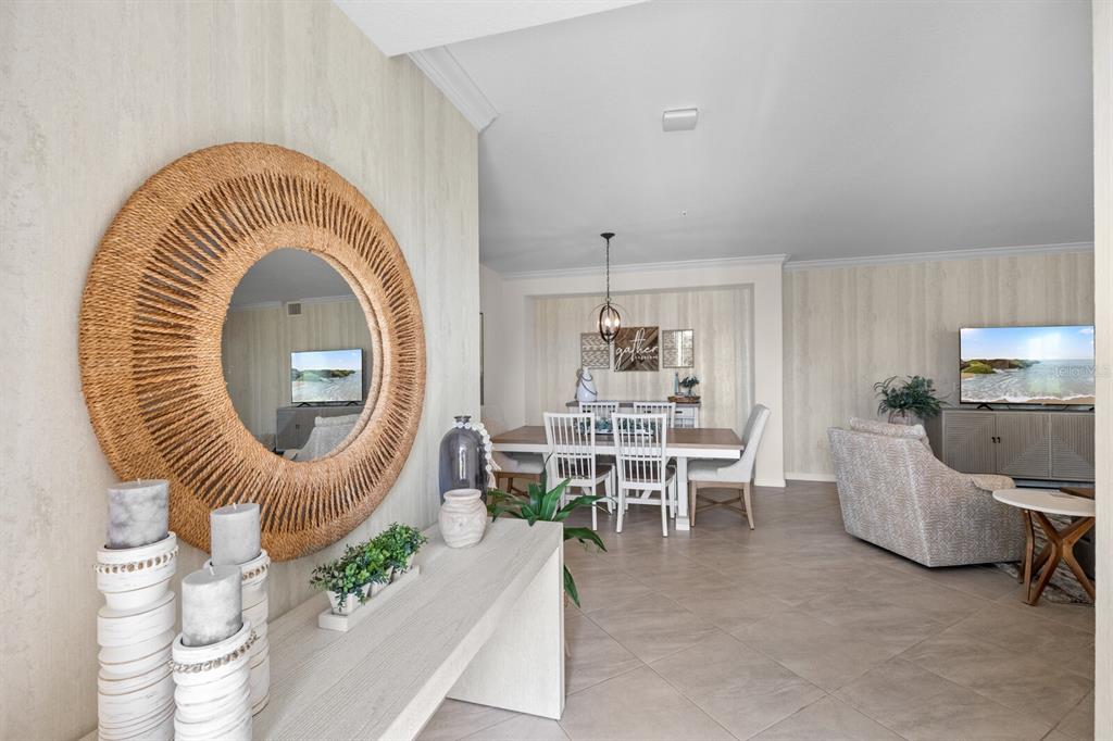 A foyer with a round mirror and console table opens into a dining and living area — 18117 GAWTHROP DRIVE UNIT 104, BRADENTON, FL