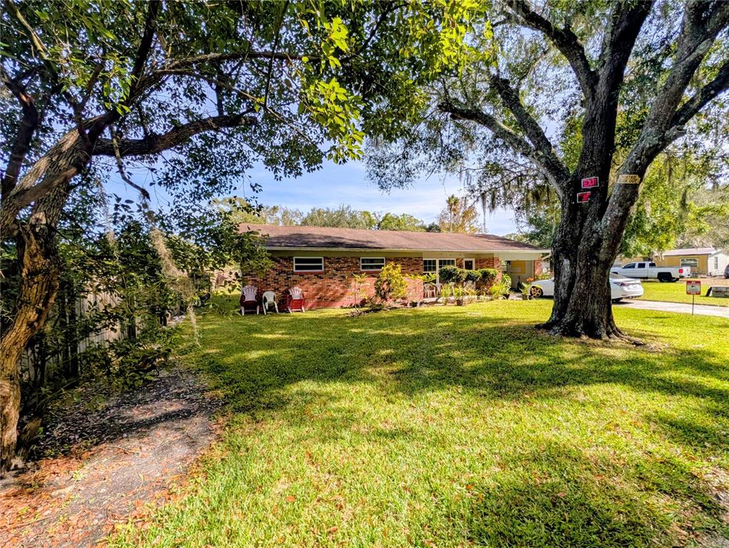 A brick ranch-style house sits on a grassy lot shaded by large oak trees — 8410 PETERSON ROAD, ODESSA, FL