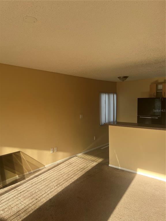 A living room with beige carpet and walls features a breakfast bar and kitchen area — 800 N FISKE BOULEVARD UNIT 711, COCOA, FL