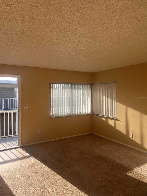 An empty room with beige carpet, tan walls, vertical blinds, and a door to a balcony — 800 N FISKE BOULEVARD UNIT 711, COCOA, FL