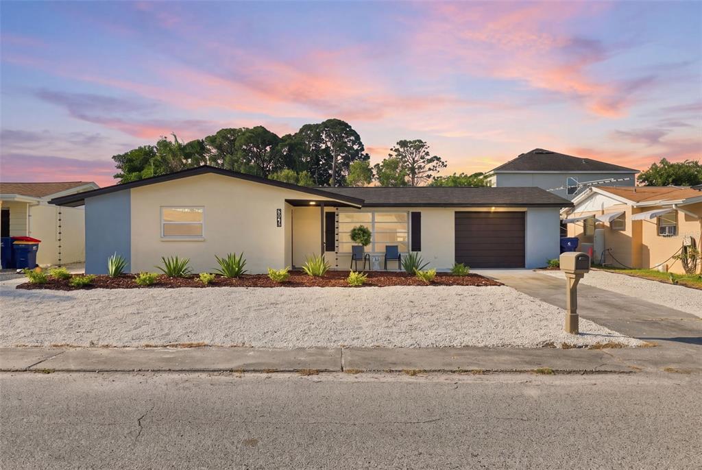 A single-story house with a light-colored exterior, a dark garage door, and a gravel yard — 3128 HARVARDSTON LOOP, HOLIDAY, FL