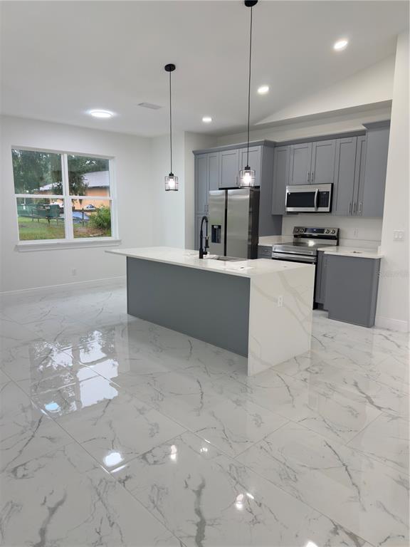 A modern kitchen features gray cabinets, a white quartz island, and white marble-patterned tile flooring — 12320 SE 70TH AVENUE, BELLEVIEW, FL