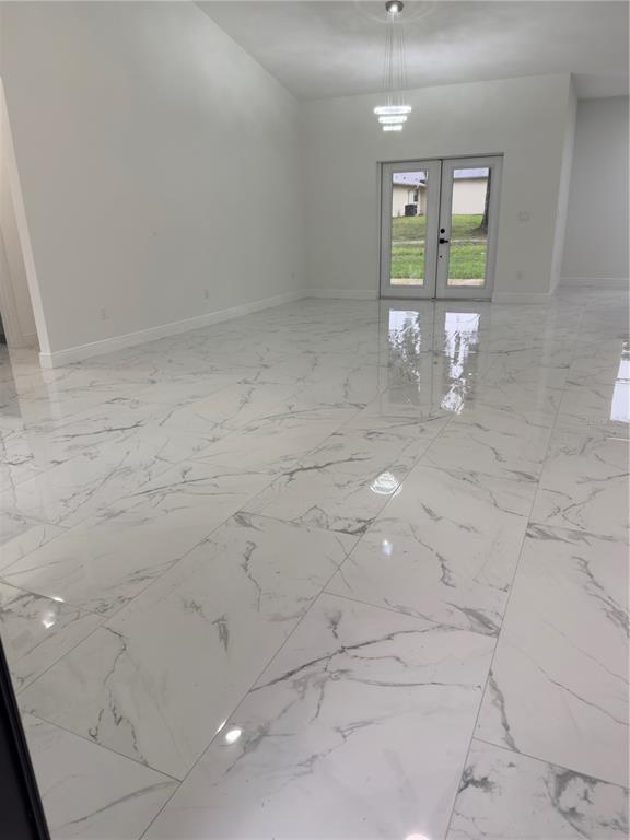 A bright room features white marble-look tile flooring and a modern chandelier near glass doors — 12320 SE 70TH AVENUE, BELLEVIEW, FL