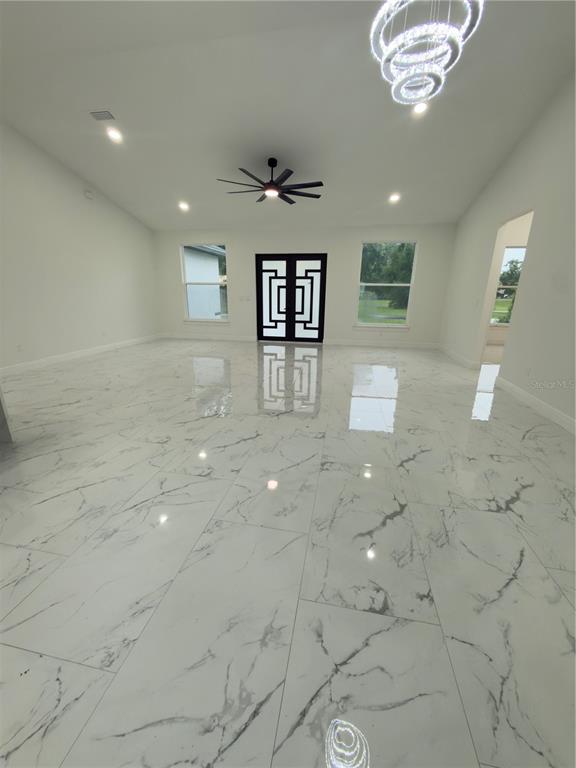A spacious room features white marble-look tile flooring, a vaulted ceiling, and a modern chandelier — 12320 SE 70TH AVENUE, BELLEVIEW, FL
