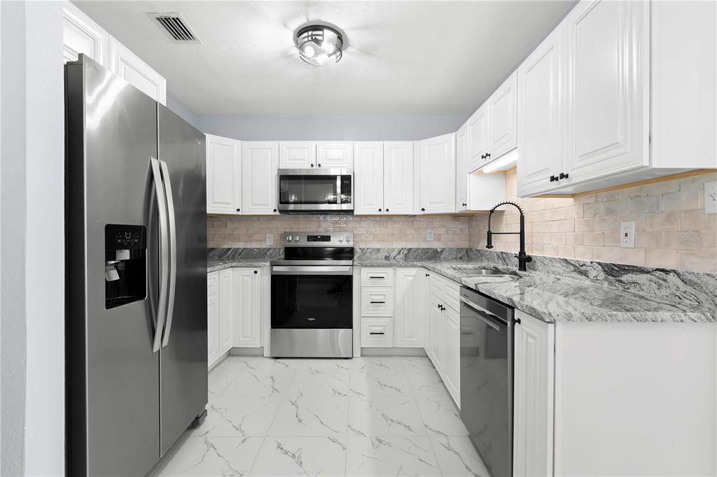 A kitchen features white cabinets, stainless steel appliances, marble-patterned countertops, and light-colored tile flooring — 3921 W GRAY STREET, TAMPA, FL