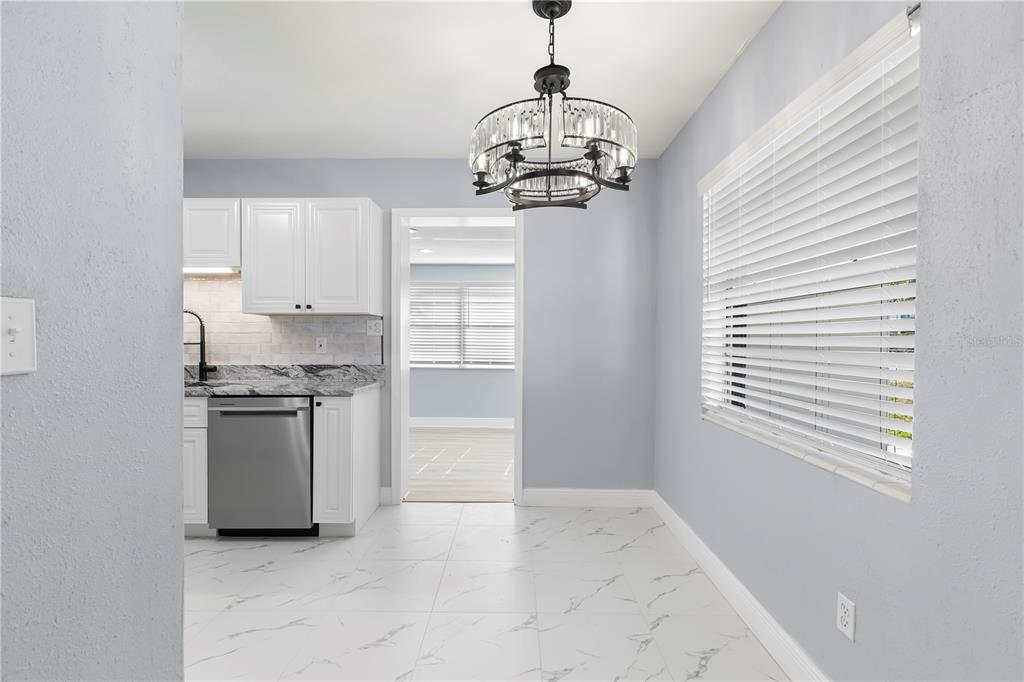A dining area with a crystal chandelier, white cabinets, stainless dishwasher, and marble-patterned tile floors — 3921 W GRAY STREET, TAMPA, FL