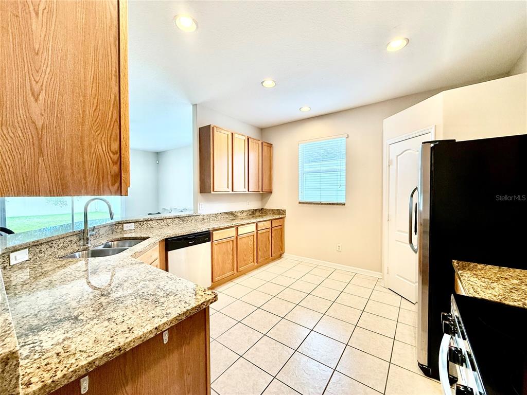 A kitchen features wood cabinets, granite countertops, a black dishwasher, and white tile flooring — 4004 LANGDRUM DRIVE, WESLEY CHAPEL, FL