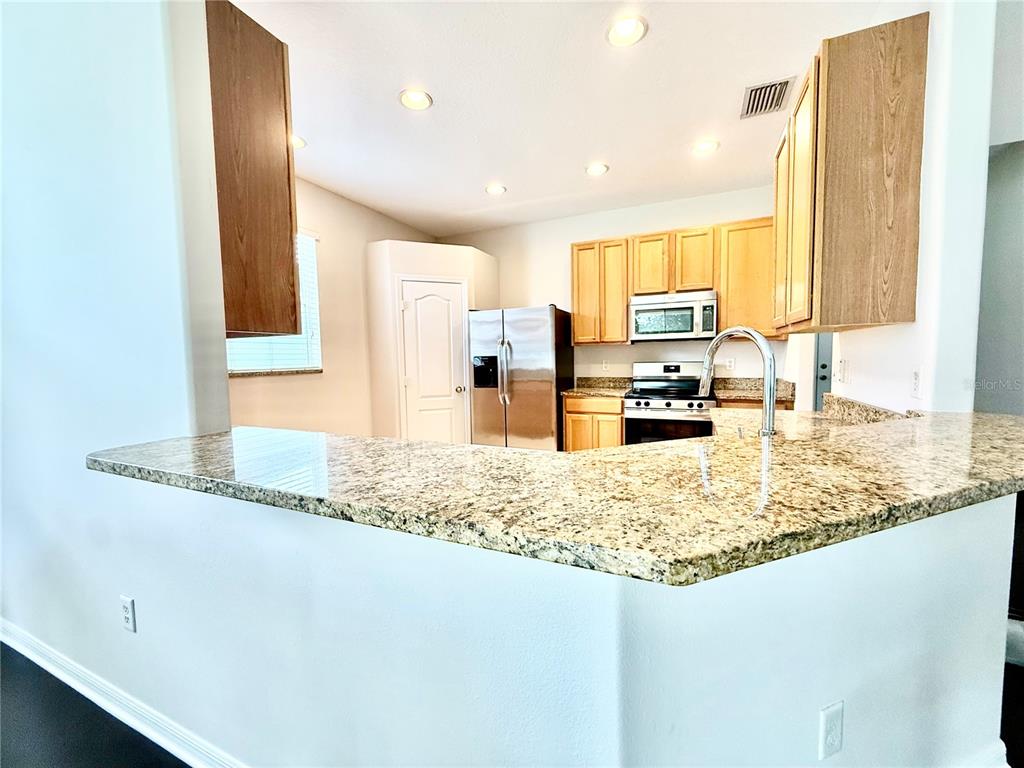 A kitchen features light wood cabinets, granite countertops, and stainless steel appliances — 4004 LANGDRUM DRIVE, WESLEY CHAPEL, FL