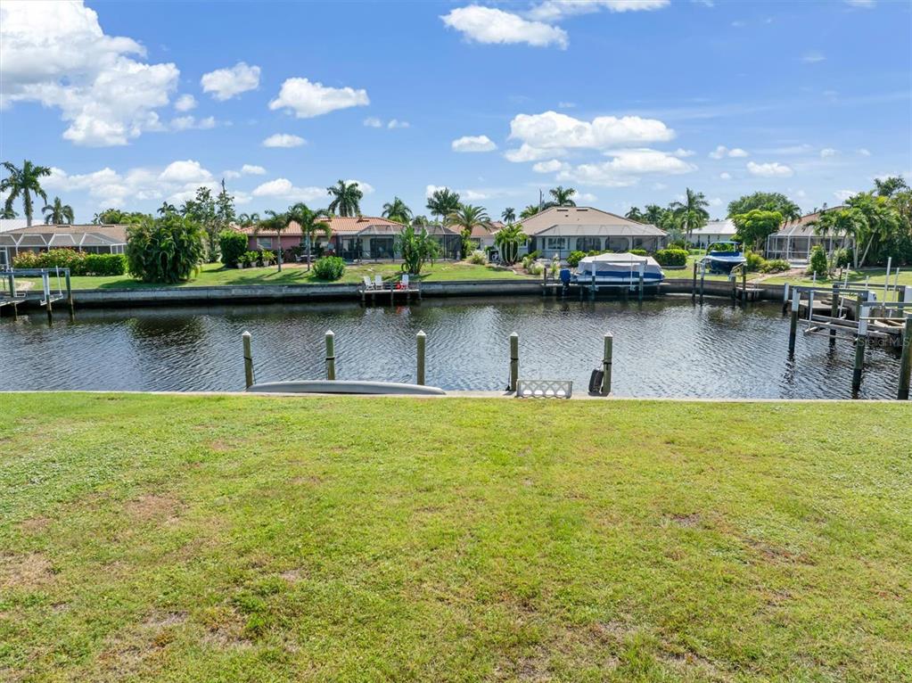 A grassy backyard overlooks a canal with boat docks and houses on the opposite bank — 834 SANTA MARGERITA LANE, PUNTA GORDA, FL