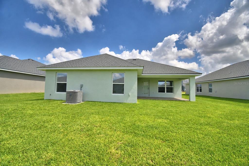 The back exterior of a light green house features a covered patio and grassy yard — 4641 CALAMINT LANE, AUBURNDALE, FL