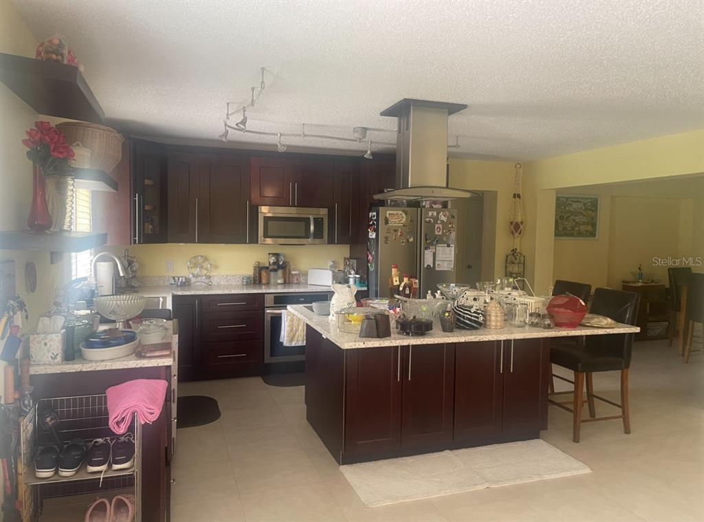 A kitchen features dark wood cabinets, granite countertops, a center island, and stainless steel appliances — 331 SHORE DRIVE E, OLDSMAR, FL