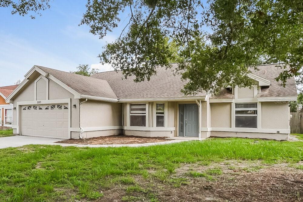 A single-story house with a beige stucco exterior, a two-car garage, and a gray roof — 2523 DOVETAIL DRIVE, OCOEE, FL