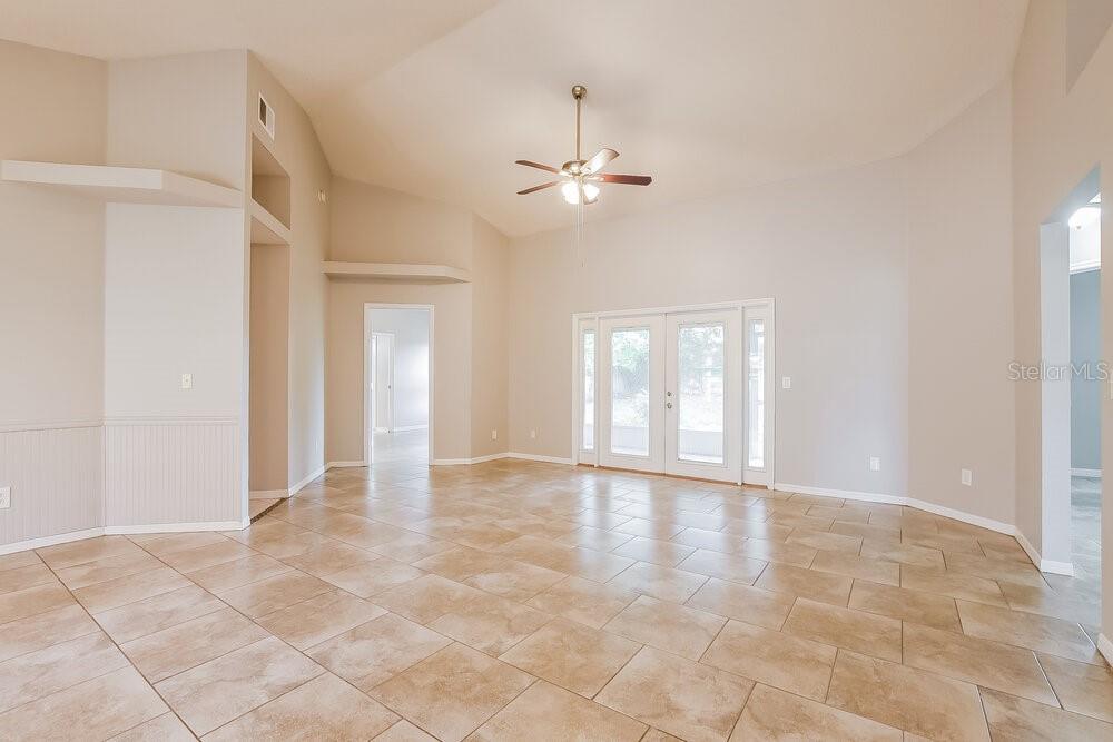 A spacious living room features light-colored tile flooring, vaulted ceilings, and glass double doors — 2523 DOVETAIL DRIVE, OCOEE, FL