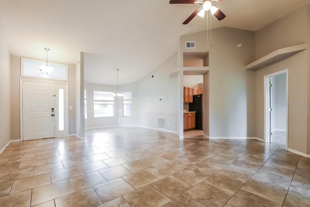 An open-concept living area features light-colored tile flooring, vaulted ceilings, and an adjacent kitchen — 2523 DOVETAIL DRIVE, OCOEE, FL