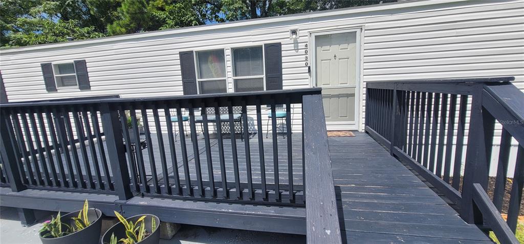 A white mobile home features a black wooden deck with stairs leading to a concrete pad — 4030 NE 212TH TERRACE, WILLISTON, FL
