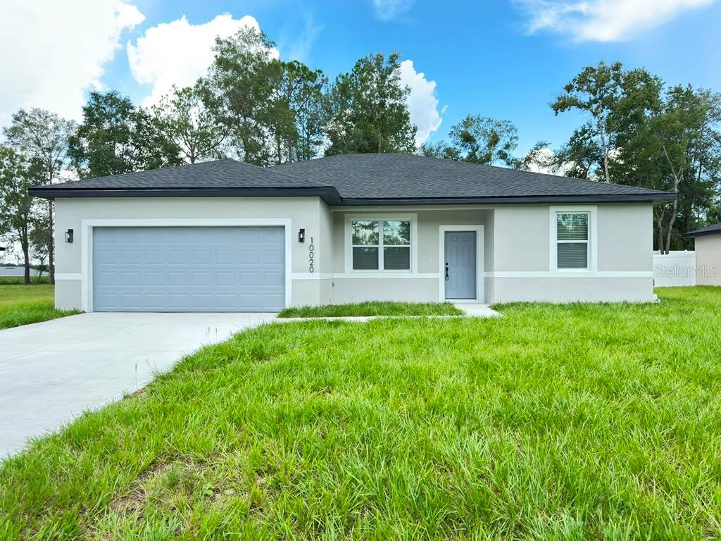 A single-story house with a gray garage door, light-colored stucco exterior, and a dark roof — 10020 N DELTONA BOULEVARD, DUNNELLON, FL