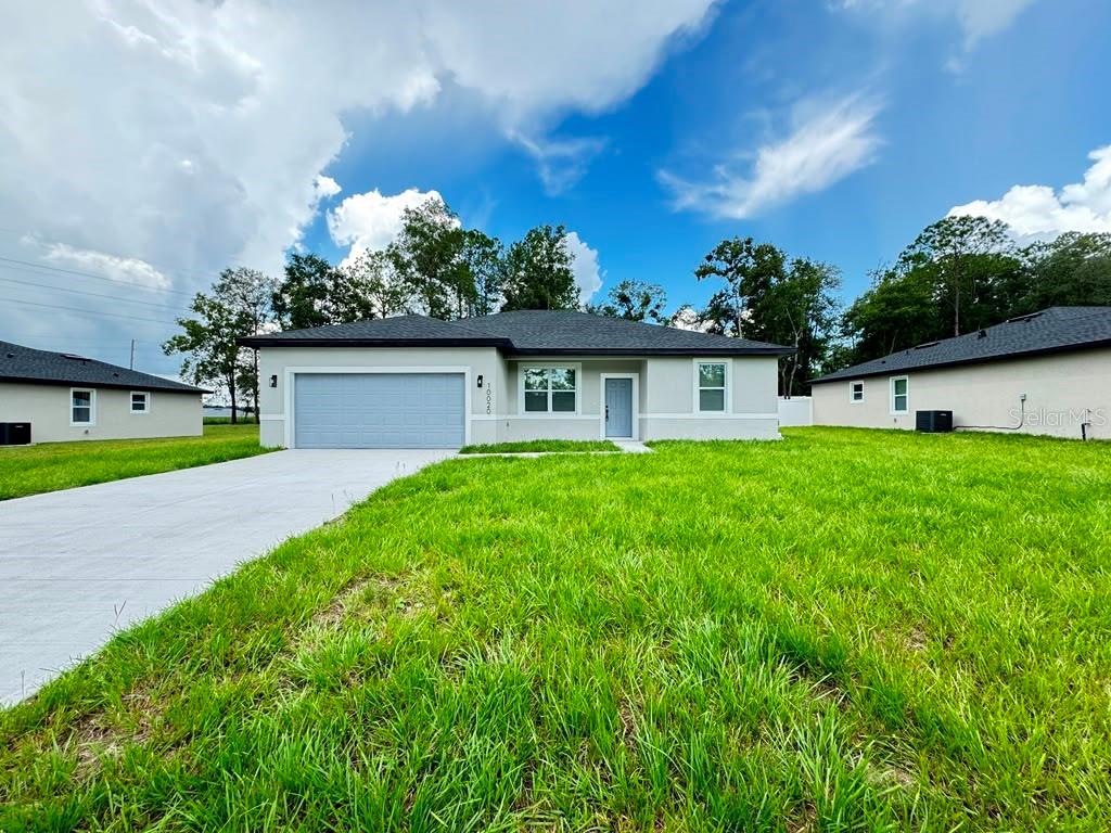 A single-story house with a gray garage, light-colored exterior, and a large front lawn — 10020 N DELTONA BOULEVARD, DUNNELLON, FL