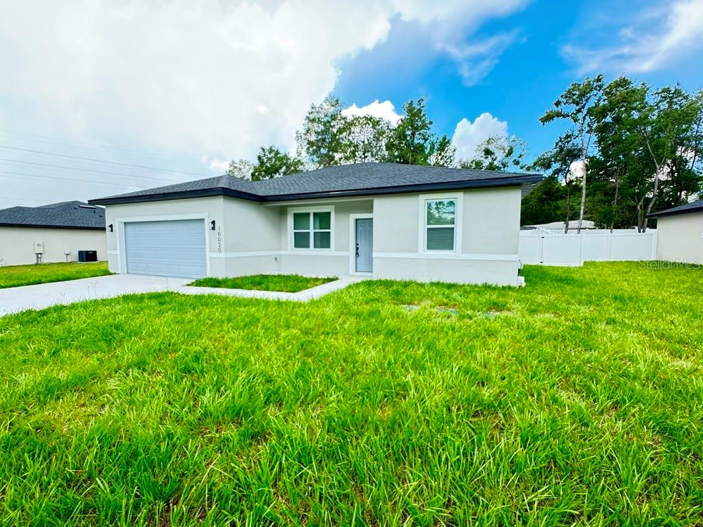 A single-story house with a light-colored stucco exterior, a gray roof, and a two-car garage — 10020 N DELTONA BOULEVARD, DUNNELLON, FL